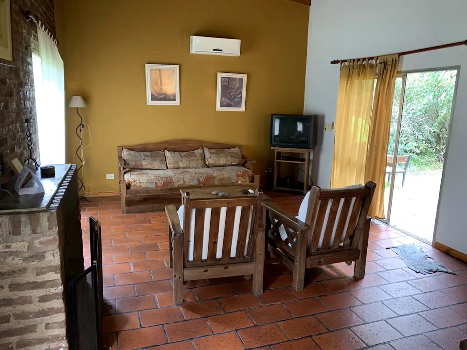 Un living, con piso de cerámica y sillones de madera.