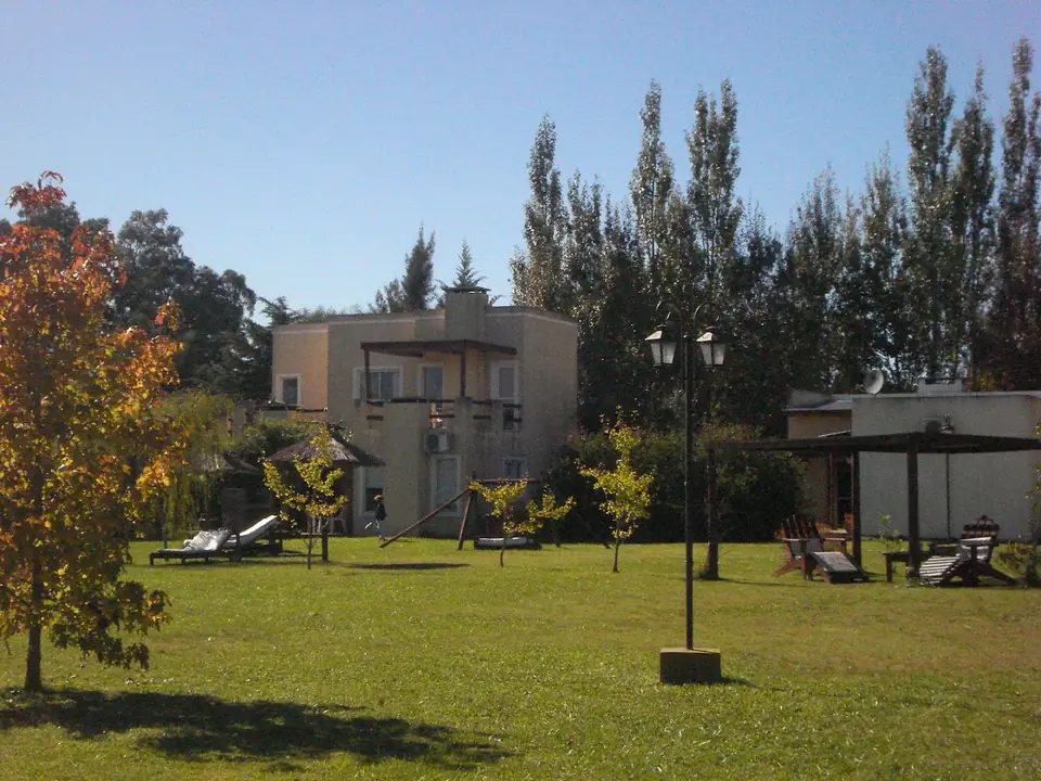 El parque con pasto y árboles, y las casas al fondo.